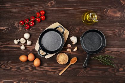 Cast iron skillets and spices on dark wooden culinary background